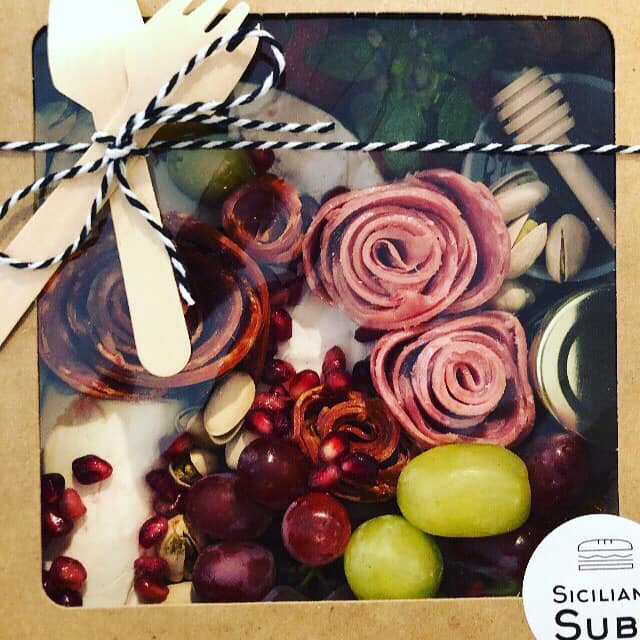 Holiday charcuterie box tied with bow and wooden serving utensils